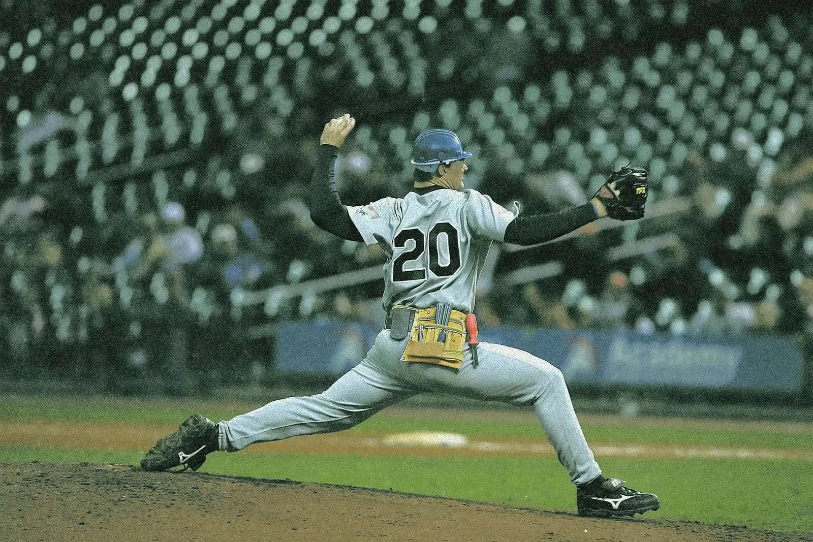 A pitcher in a hard hat and a tool belt, mid-throw, in the same grainy, faded treatment