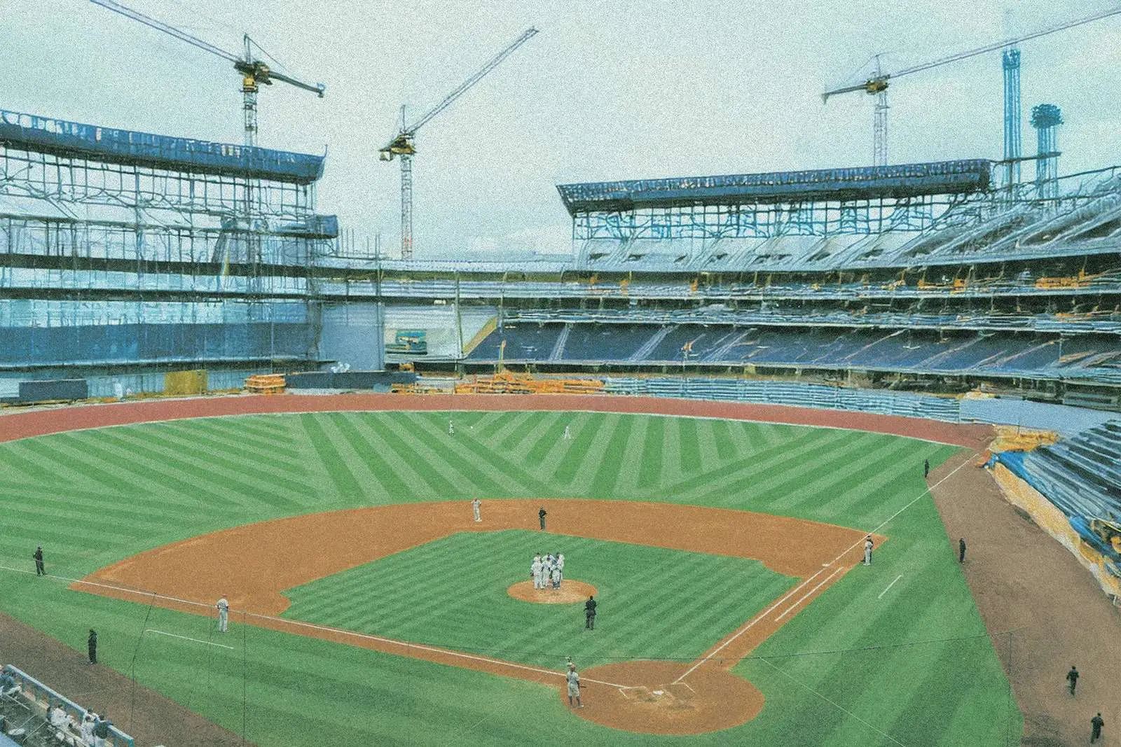 A ballpark under construction, cranes over the stands, in Silo In’s grainy, faded image treatment
